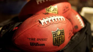 Mehrere American Football Bälle liegen in einer schwarzen Tasche