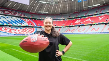 Nadine Nurasyid steht neben dem Rasen in der Allianz Arena und hält einen Football in der rechten Hand