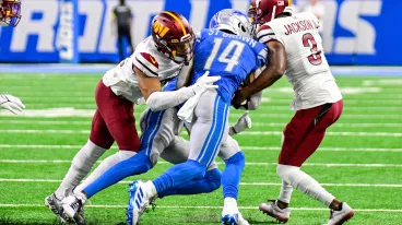 Amon-Ra St. Brown wird bei einem NFL Spiel von zwei Gegnern getackelt