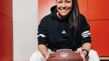 Nadine Nurasyid sitzt mit einem Football in der Hand auf einer Bank in einer Umkleidekabine