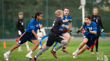 Mehrere Jugendliche spielen Flag Football auf einem Rasenplatz