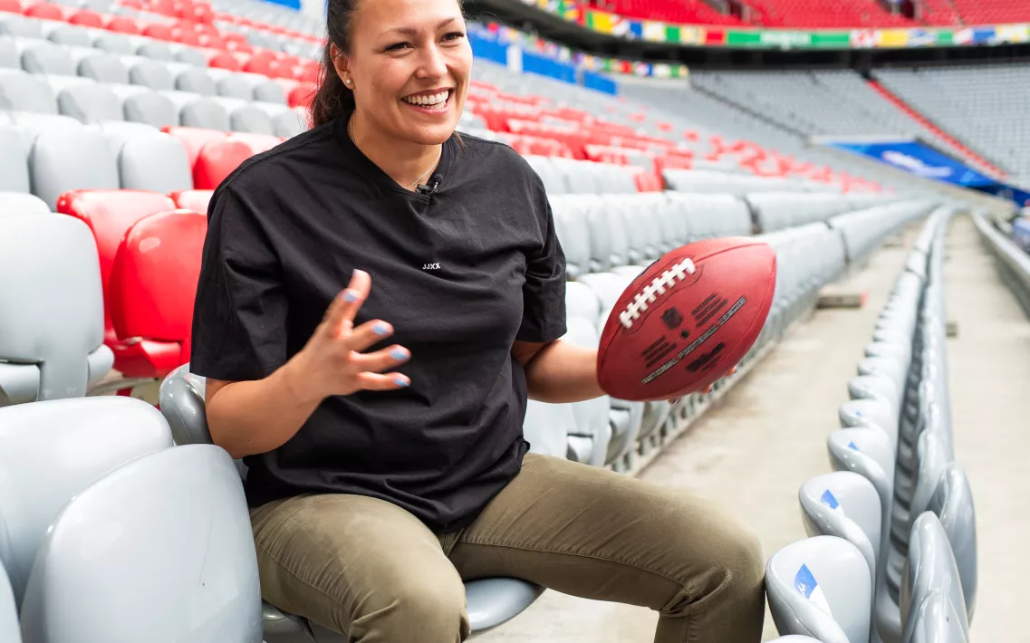 Nadine Nurasyid sitzt auf der Tribüne in der Allianz Arena und hält einen Football in ihrer linken Hand