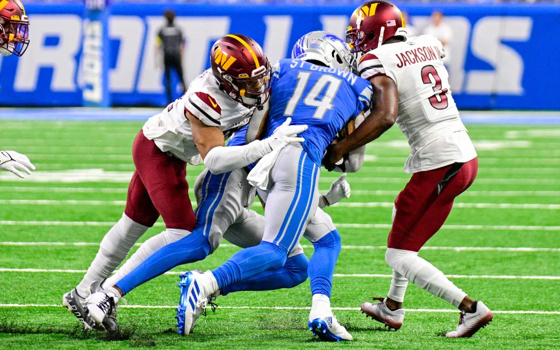 Amon-Ra St. Brown wird bei einem NFL Spiel von zwei Gegnern getackelt